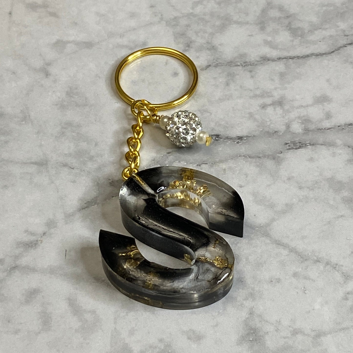 Letter S of The Clear Resin Alphabet Letter Keychain with Gold Flake and Black Accents