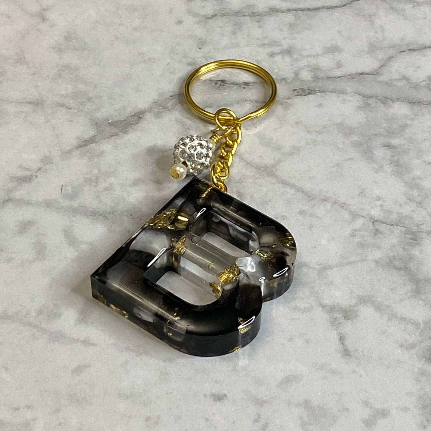 Letter B of The Clear Resin Alphabet Letter Keychain with Gold Flake and Black Accents
