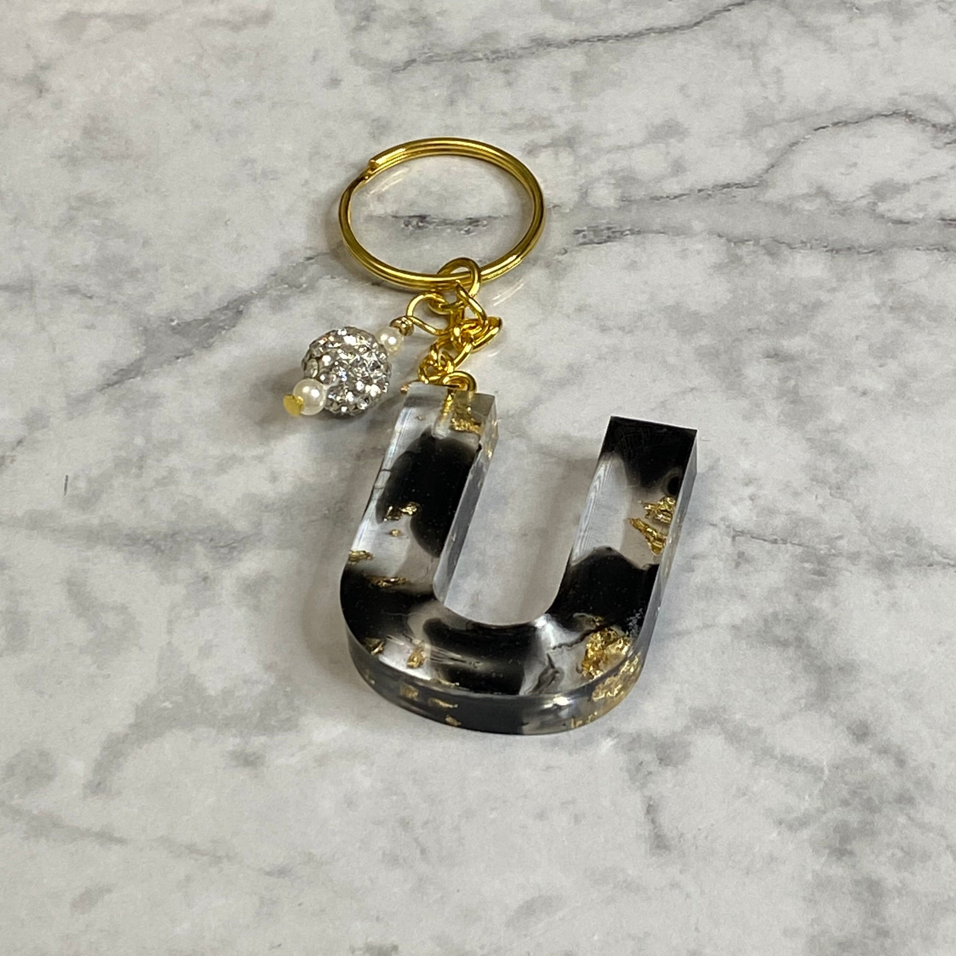 Letter U of The Clear Resin Alphabet Letter Keychain with Gold Flake and Black Accents