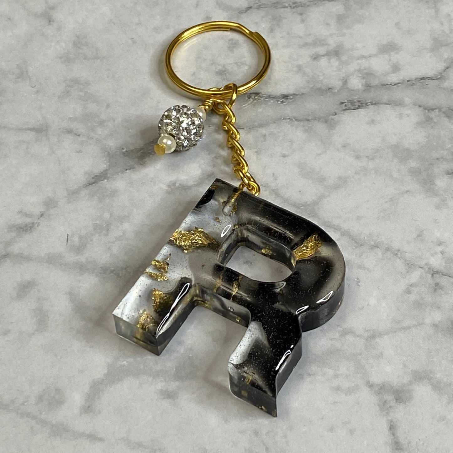 Letter R of The Clear Resin Alphabet Letter Keychain with Gold Flake and Black Accents