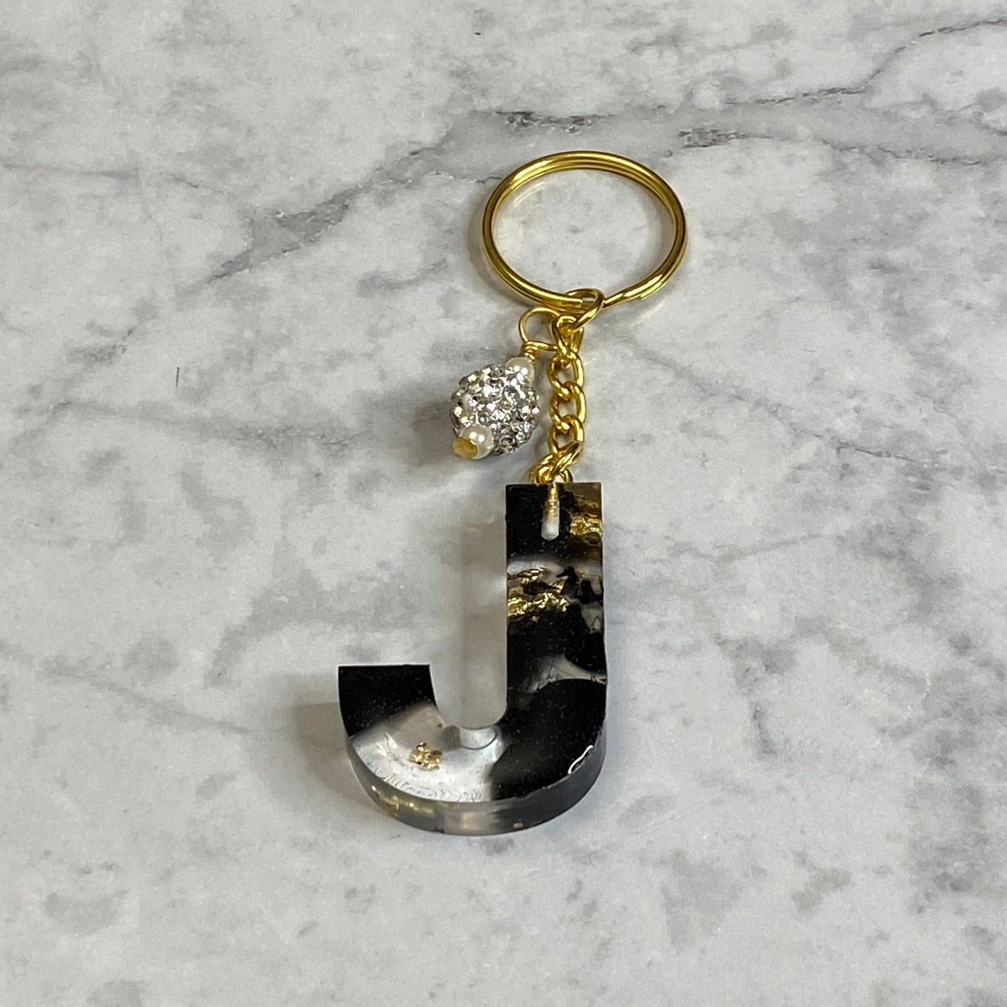 Letter J of The Clear Resin Alphabet Letter Keychain with Gold Flake and Black Accents