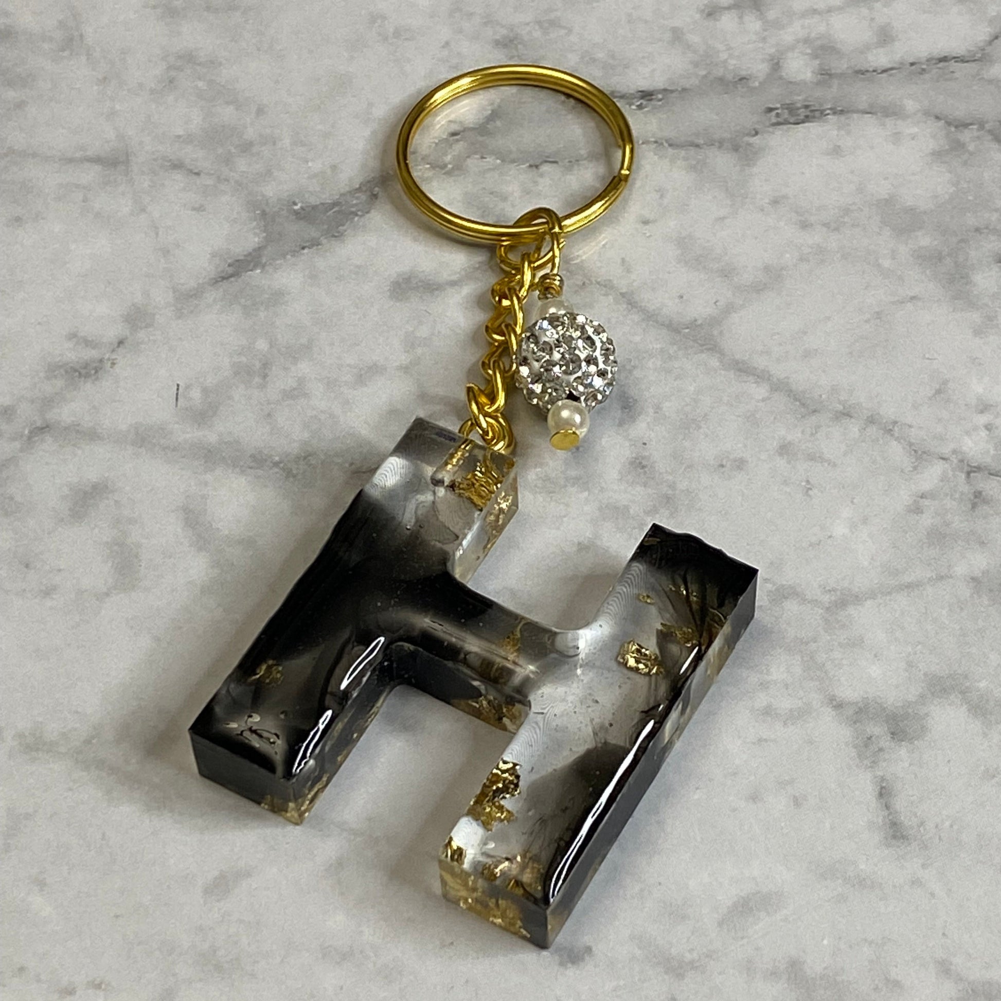 Letter H of The Clear Resin Alphabet Letter Keychain with Gold Flake and Black Accents