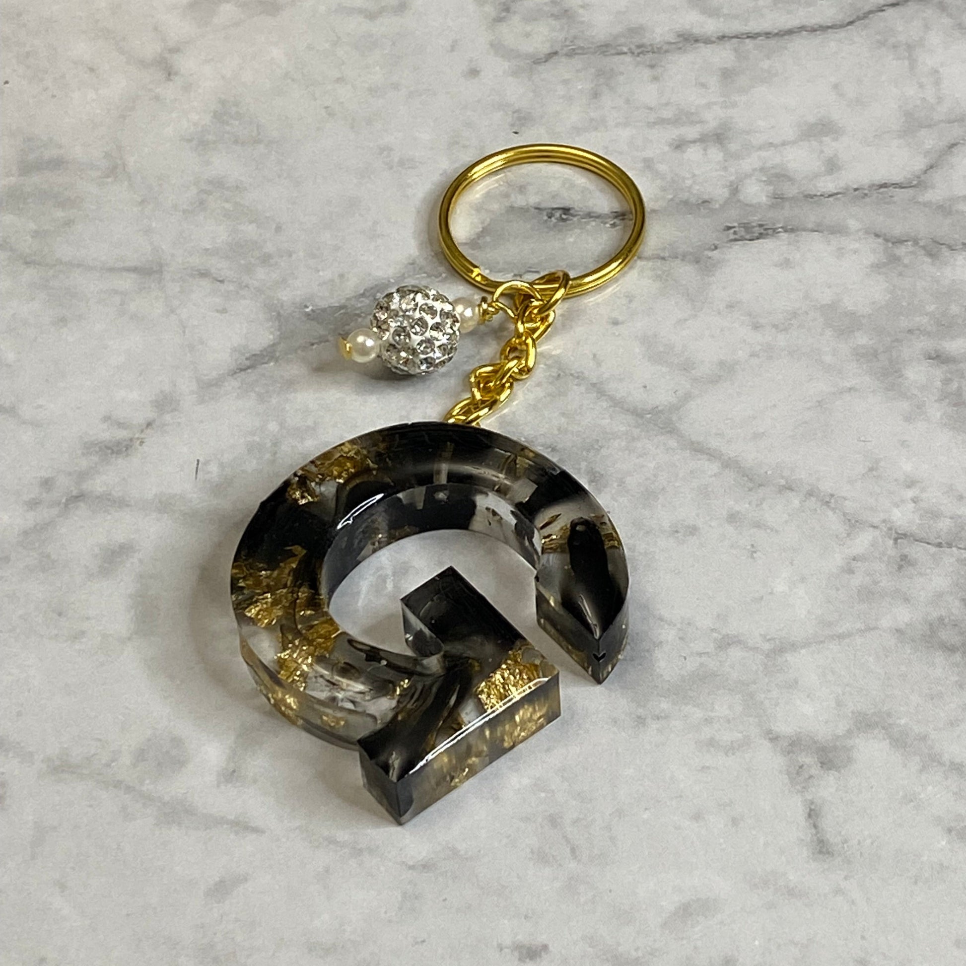 Letter G of The Clear Resin Alphabet Letter Keychain with Gold Flake and Black Accents