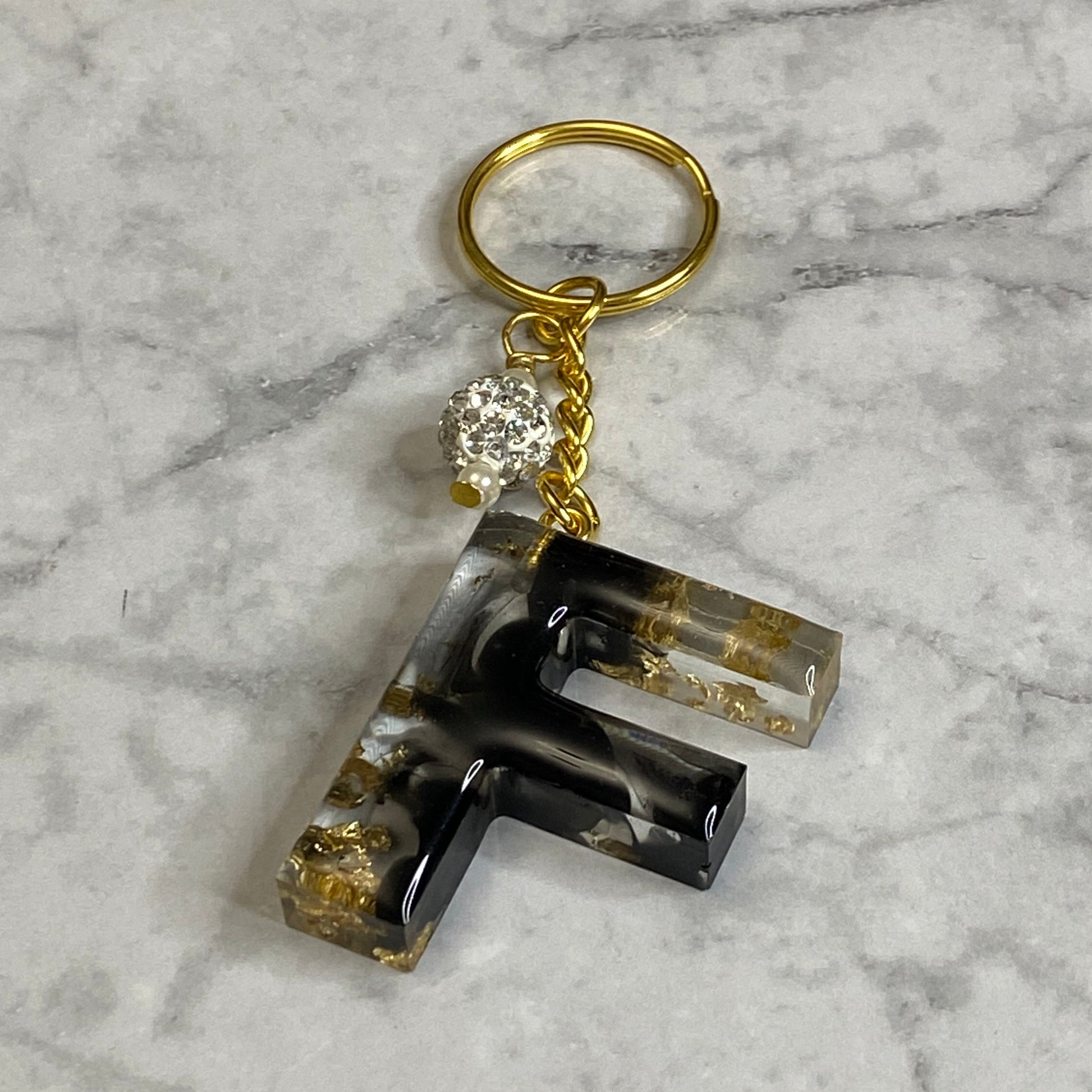 Letter F of The Clear Resin Alphabet Letter Keychain with Gold Flake and Black Accents