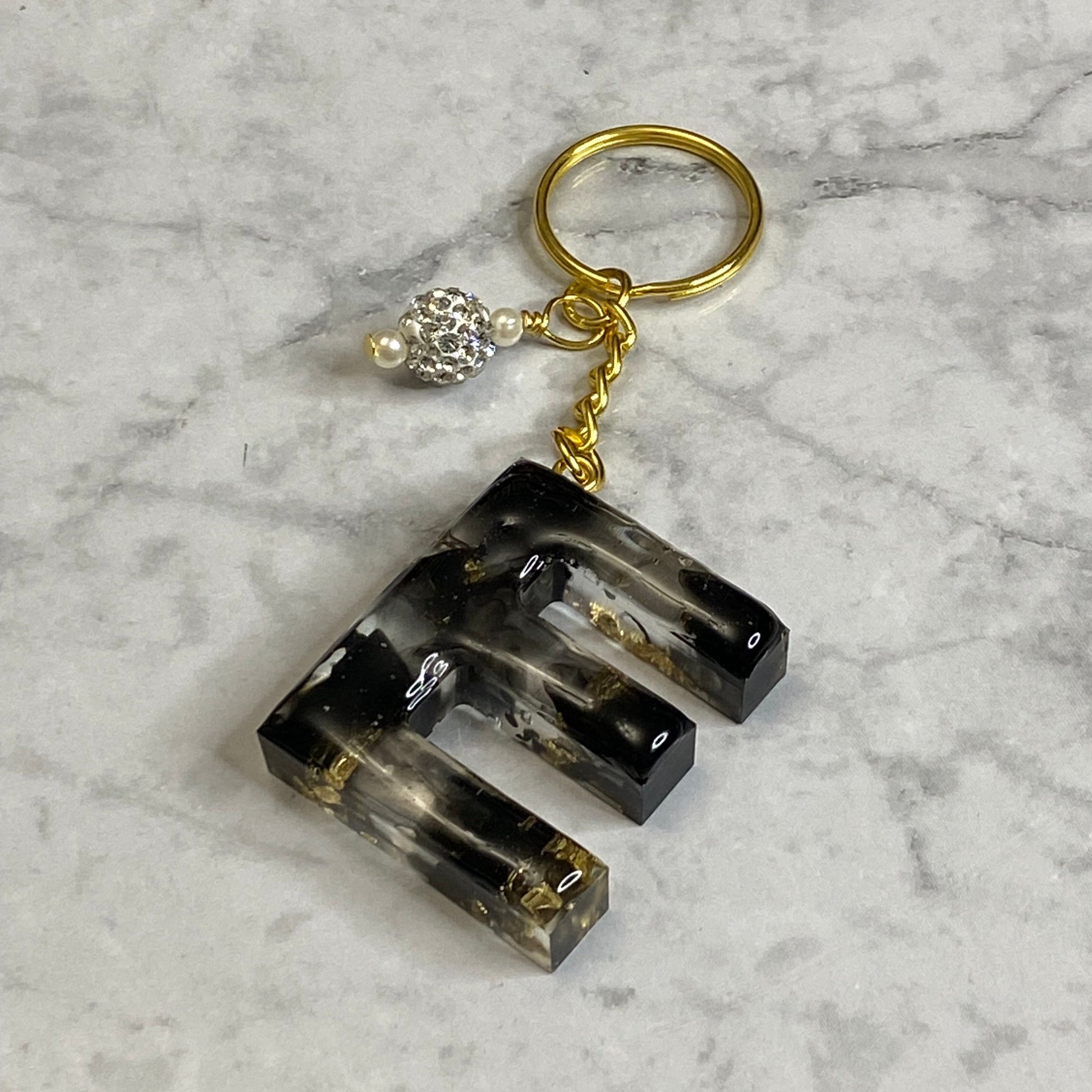 Letter E of The Clear Resin Alphabet Letter Keychain with Gold Flake and Black Accents