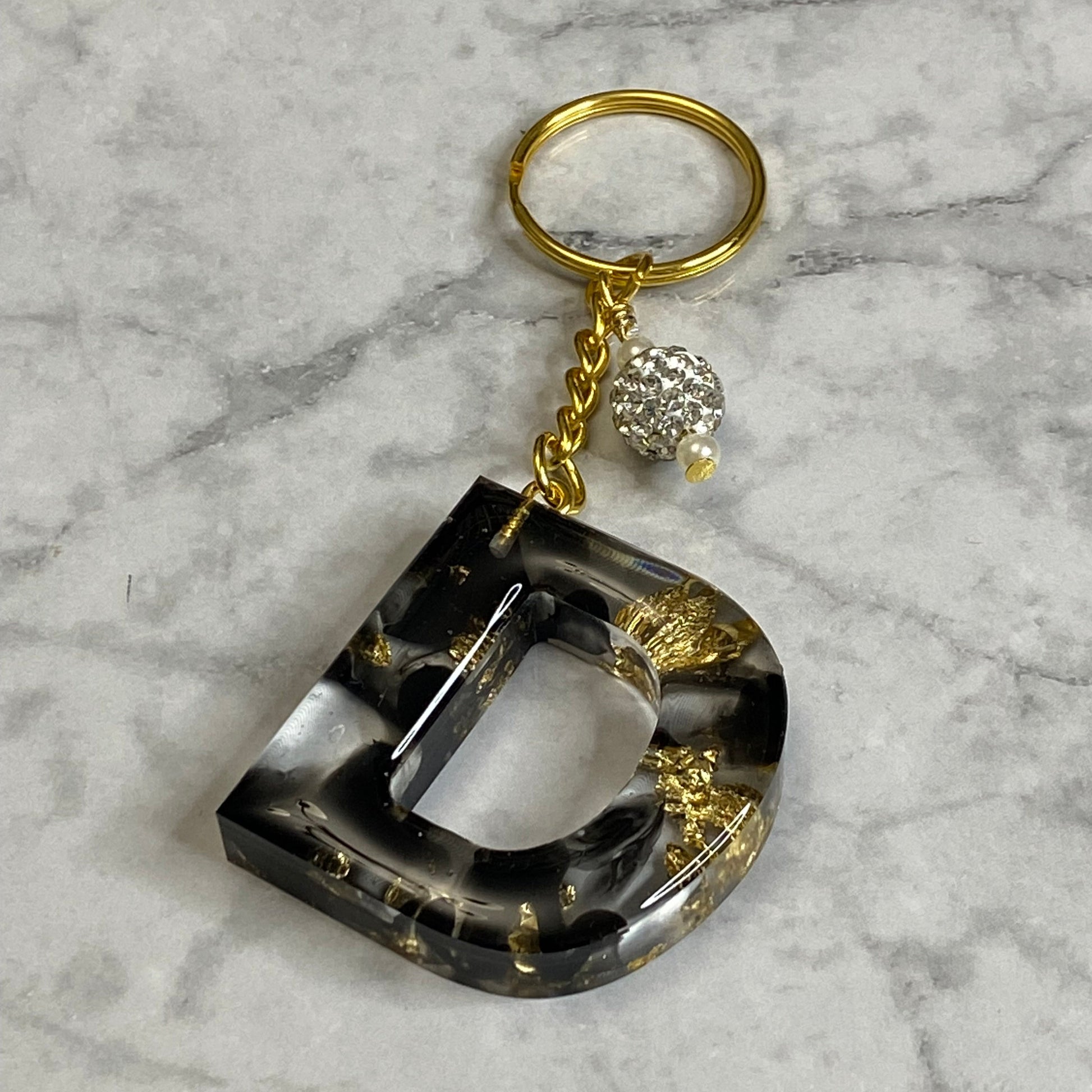 Letter D of The Clear Resin Alphabet Letter Keychain with Gold Flake and Black Accents